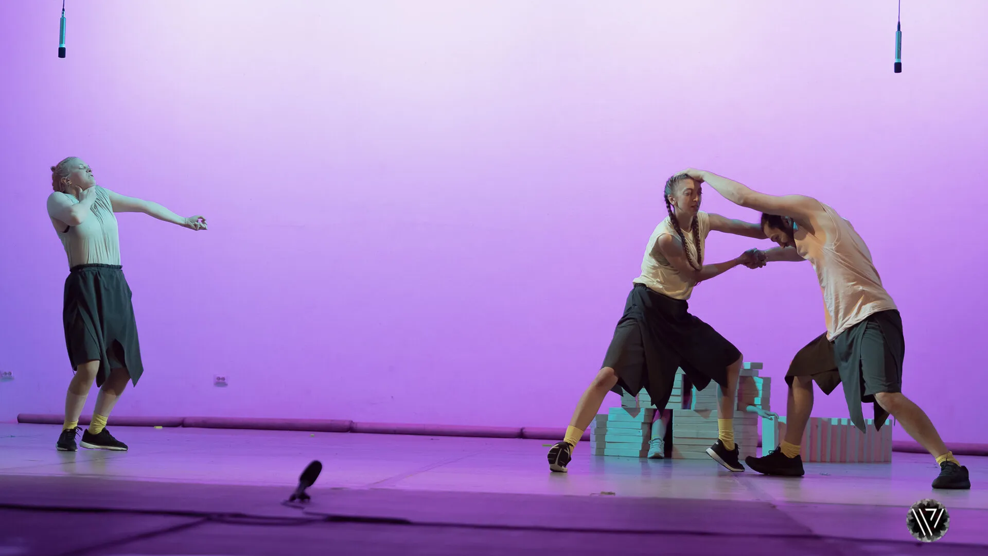 Three performers on a stage washed in purple light