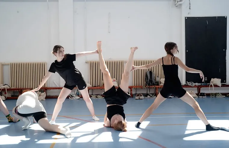 Three dancers balancing in wide shapes in a school gym